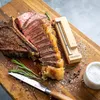 A cooked steak is sliced and presented on a wooden cutting board with a meat thermometer, knife, and salt. Náhled obrázku produktu