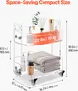 A clear acrylic rolling cart with two shelves, displaying various bathroom or vanity items. Produktbild-Vorschau