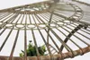 Close-up view of a decorative metal table with a distressed finish, showing intricate wirework and a hint of greenery from a plant inside. Produktbild-Vorschau