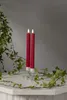 Two red LED taper candles with a flame effect, placed in clear candle holders on a white surface, with green ivy vines draped around them. Produktbild-Vorschau