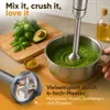 An immersion blender is used to make a green puree in a pot, with basil and avocado on a wooden cutting board in the background. Produktbild-Vorschau