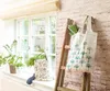 A tote bag with a floral pattern hangs on a wooden ladder next to a window with plants. Anteprima dell’immagine prodotto
