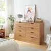 A bedroom scene featuring a wooden dresser with drawers, a lamp, plants, and artwork. Produktbild-Vorschau