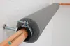 A close-up view of a copper pipe insulated with gray foam and secured with a clamp and bolt to a white wall. Produktbild-Vorschau
