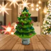 A ceramic Christmas tree night light sits on a wooden table in front of a blurred background with Christmas lights and decorations. Náhľad obrázku produktu