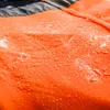 Close-up of orange fabric with water droplets on it, with some black and gray fabric visible at the top. Produktbild-Vorschau