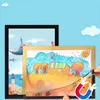 Two magnetic picture frames are shown, one black and one gold, displaying children's drawings. The gold frame is being held open by hands, revealing a magnet and a drawing inside. The background is a light blue with cartoon clouds. Anteprima dell’immagine prodotto