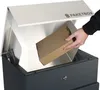 A hand is placing a cardboard box into a dark grey parcel box with a silver lid. Produktbild-Vorschau