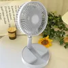 A white foldable desk fan is placed on a table next to a candle and some greenery. Náhled obrázku produktu