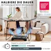 A woman is hanging laundry on a drying rack, with a device underneath that appears to be a dryer. The scene is set in a living room. Produktbild-Vorschau