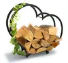 A heart-shaped metal firewood rack filled with logs, decorated with a green vine. Produktbild-Vorschau