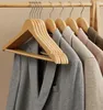 Several wooden hangers with clothes hanging on them are displayed on a wooden rack. Náhled obrázku produktu
