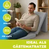 A man is reading a book while sitting on a folded mattress in a living room. Produktbild-Vorschau