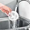 A hand is holding a white mesh filter under a running faucet in a stainless steel sink. Produktbild-Vorschau