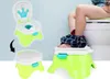 A child's legs are visible as they sit on a child's potty training seat, which is placed next to a larger toilet. Two other views of the potty training seat are shown to the left, one with the lid open and the other with the lid closed. Produktbild-Vorschau