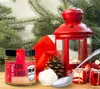 A Christmas-themed still life featuring a jar of egg liqueur, a red lantern, pine cones, and gift boxes. Produktbild-Vorschau