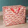 A large, patterned storage bag with red handles sits on a wooden floor against a teal wall. Produktbild-Vorschau