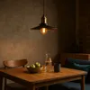 A vintage-style pendant light hangs above a wooden dining table set with a bowl of apples, a carafe of water, and a mug. Podgląd zdjęcia produktu