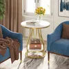 A round side table with two shelves, decorated with sunflowers and books, placed between two blue armchairs in a living room setting. Produktbild-Vorschau