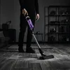 A person is using a cordless vacuum cleaner on a carpeted floor in a dimly lit room. Voir les images du produit