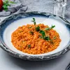 A close-up of a bowl of fregola pasta with tomato sauce and zucchini, garnished with fresh herbs. Produktbild-Vorschau