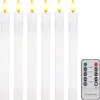 Six white LED candles with flickering yellow and orange flames are arranged in a row. A remote control is placed to the right of the candles. Podgląd zdjęcia produktu