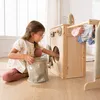A young girl is playing with a wooden toy washing machine, putting clothes into the drum. Produktbild-Vorschau