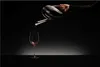 A hand is pouring red wine from a decanter into a wine glass against a dark background. Náhled obrázku produktu