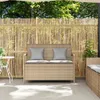 A garden bench with storage and cushions is placed on a patio in front of a bamboo fence, with trees and foliage in the background. Náhľad obrázku produktu