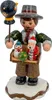 Ein handgefertigter Holzfigur zeigt einen Spielwarenhändler mit einem Tablett voller bunter Spielzeuge in den Händen und einem Vogel auf einem Stock während er auf einem schneebedeckten Sockel steht Produktbild-Vorschau