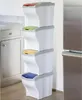 A stack of four BAMA Papierkorb POKER 20L bins with different colored lids, placed in a kitchen setting next to a refrigerator and cabinets. Náhľad obrázku produktu