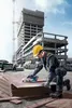 A construction worker using a circular saw on a stack of plywood at a construction site. Produktbild-Vorschau