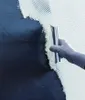 A gloved hand is using a trowel to spread white adhesive onto a dark surface. Produktbild-Vorschau