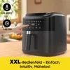 A hand is shown interacting with the control panel of a black air fryer, which is placed on a wooden countertop. The background is a kitchen setting. Produktbild-Vorschau
