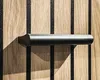 A close-up shot of a black handle on a wooden surface with black vertical stripes. Produktbild-Vorschau