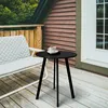 A black metal side table with a cup of coffee on it, placed on a wooden deck next to a bench. Produktbild-Vorschau