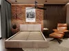 A bedroom scene with a bed, chair, and wall decor. Produktbild-Vorschau