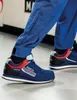 A person wearing blue work pants and Sparco Martini Racing shoes, walking on a light gray floor. Podgląd zdjęcia produktu