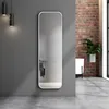 A full-length mirror is leaning against a gray wall, reflecting a bathroom scene. To the right, a brick wall and a potted plant are visible. Voir les images du produit