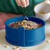 A person is decorating a cake with pistachios in a blue springform pan. Produktbild-Vorschau