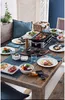A table set for a raclette meal with a raclette grill in the center, surrounded by plates of food, salads, and drinks. Anteprima dell’immagine prodotto