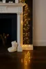 Fairy lights draped over a fireplace hearth, with a pair of fluffy slippers nearby. Produktbild-Vorschau