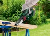 A person is using a cordless chainsaw to cut a piece of wood outdoors. Produktbild-Vorschau