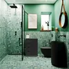 A modern bathroom with green terrazzo walls and floor, featuring a black vanity, toilet, sink, and shower. Podgląd zdjęcia produktu