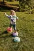 A young child is playing on a grassy hill, stepping on colorful stacking stones. Anteprima dell’immagine prodotto