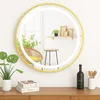 A round LED mirror with a gold frame is displayed on a wooden dresser, reflecting a room with a chair and a shelf. Podgląd zdjęcia produktu