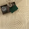 A close-up overhead view of a rug with a geometric pattern, featuring a wooden tray with a candle, a small vase with dried flowers, and a green book. Produktbild-Vorschau