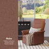 A recliner chair with a throw blanket and pillow, placed in a living room setting with a window view of a garden and a bookshelf. Náhled obrázku produktu
