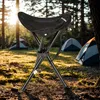 A black camping stool is set up in a forest clearing with tents in the background. Produktbild-Vorschau