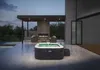 An Intex Pure Spa Greystone Deluxe hot tub is set up on a modern patio at dusk, next to a swimming pool and a contemporary house with a fireplace. Náhľad obrázku produktu
